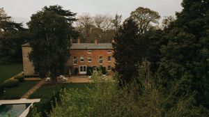 Brick mansion of Aswarby Rectory with large gardens and tall trees viewed from above on an overcast day.
