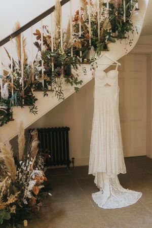 A white lace wedding dress hangs from a staircase banister adorned with greenery and floral decorations at Aswarby Rectory.