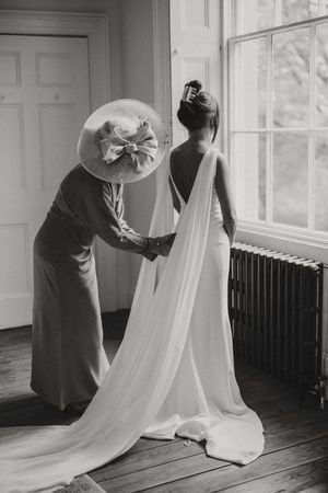 A black and white photograph showing an elegant wedding dress being adjusted near a bright window at Aswarby Rectory.