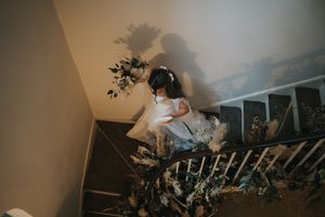Bride descends a staircase casting dramatic shadows against a beige wall in moody lighting at Aswarby Rectory.