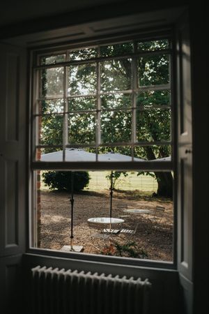 View through a white framed window looking out at a tree-lined yard with an empty swing in the sunlight at Aswarby Rectory.