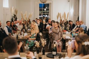 Wedding reception guests seated at long tables in a bright white venue with pampas grass decorations at Aswarby Rectory.
