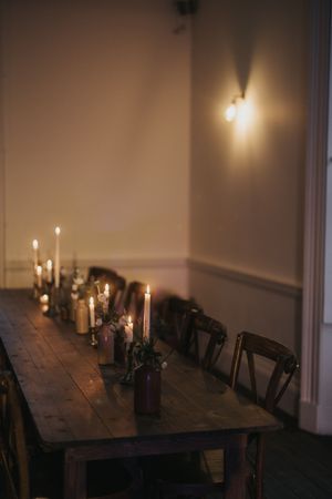 Lit candles illuminate a rustic wooden dining table in a dimly lit room with dark wooden chairs at Aswarby Rectory.