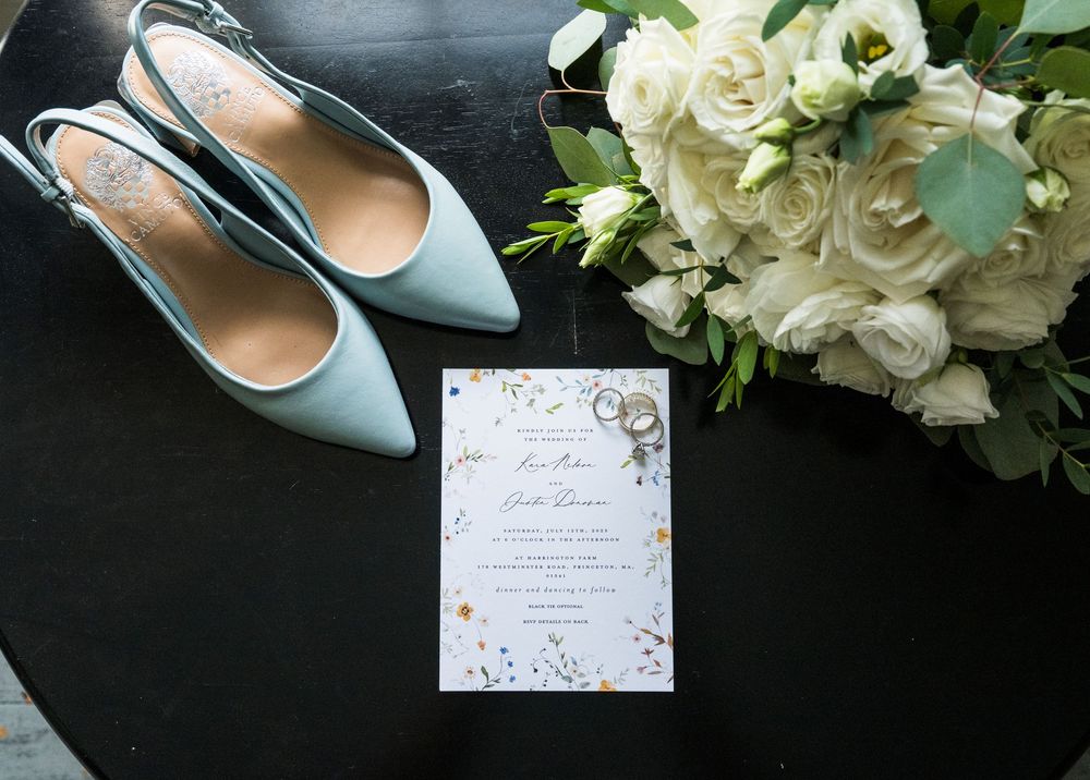 Wedding details including white flowers, blue shoes, and handwritten invitation on dark background.