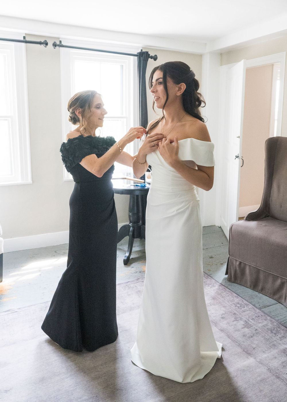 Candid moments during a wedding as two people in black and white dresses prepare in a bright room.