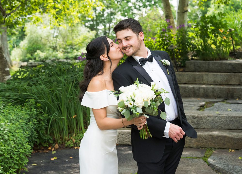Couple sharing romantic moments in a lush green garden setting with white flowers.