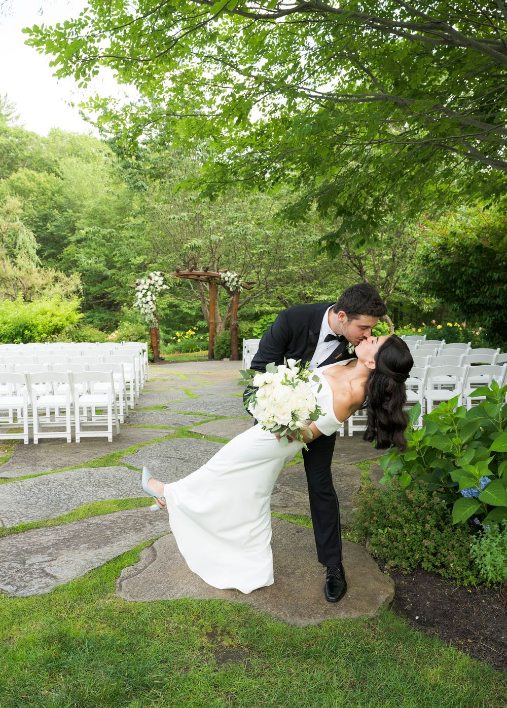 Wedding photoshoot in a scenic garden path with white chairs and greenery.