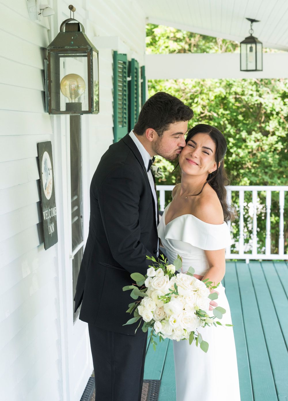 Wedding couple embracing on white porch with turquoise benches and lanterns.