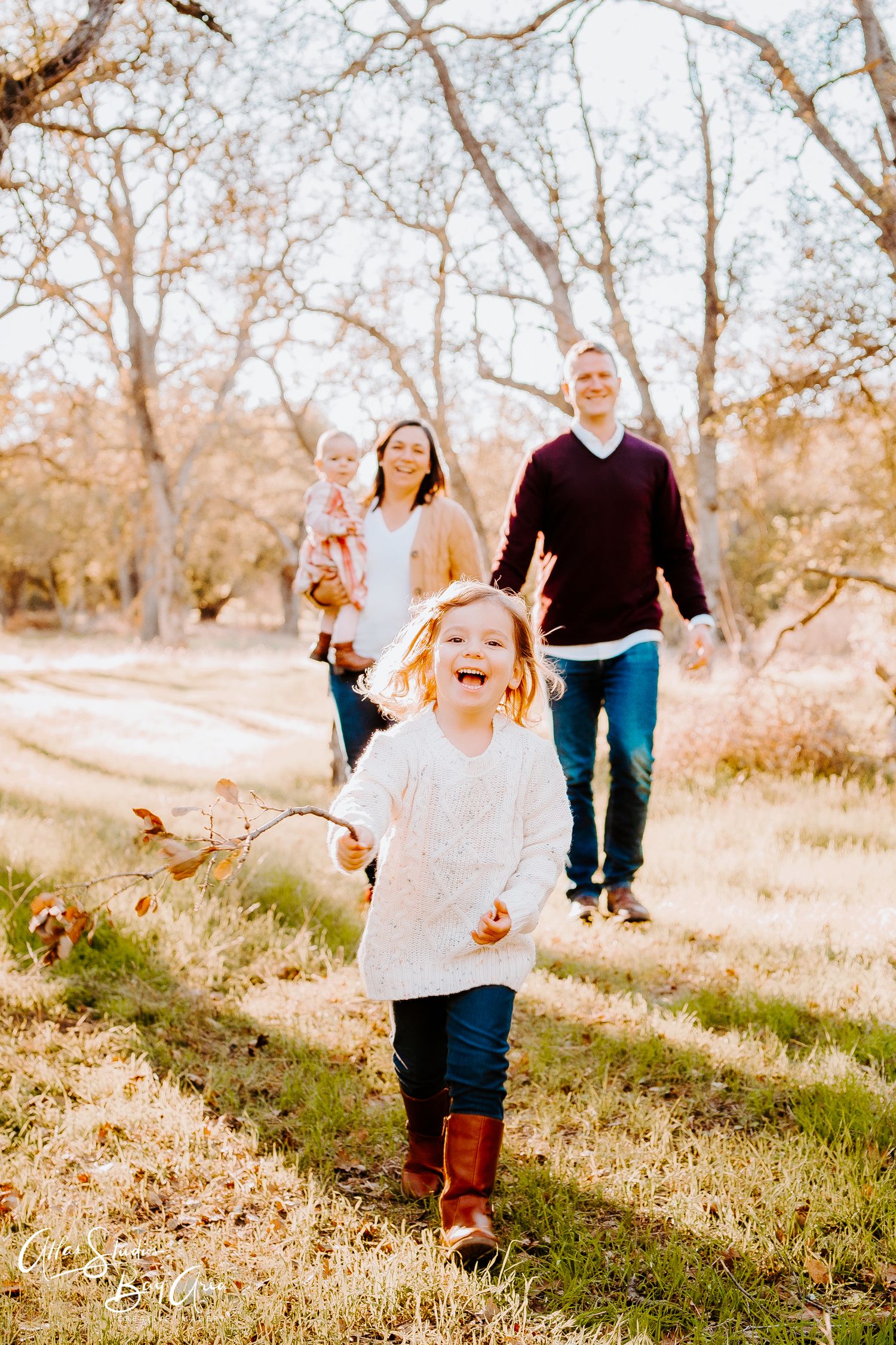Family walking together on autumn path while child runs joyfully ahead.