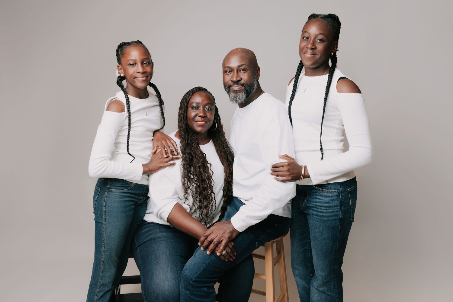 Smiling family of four poses in matching white tops and jeans against a neutral background for a studio portrait in Basildon, Essex