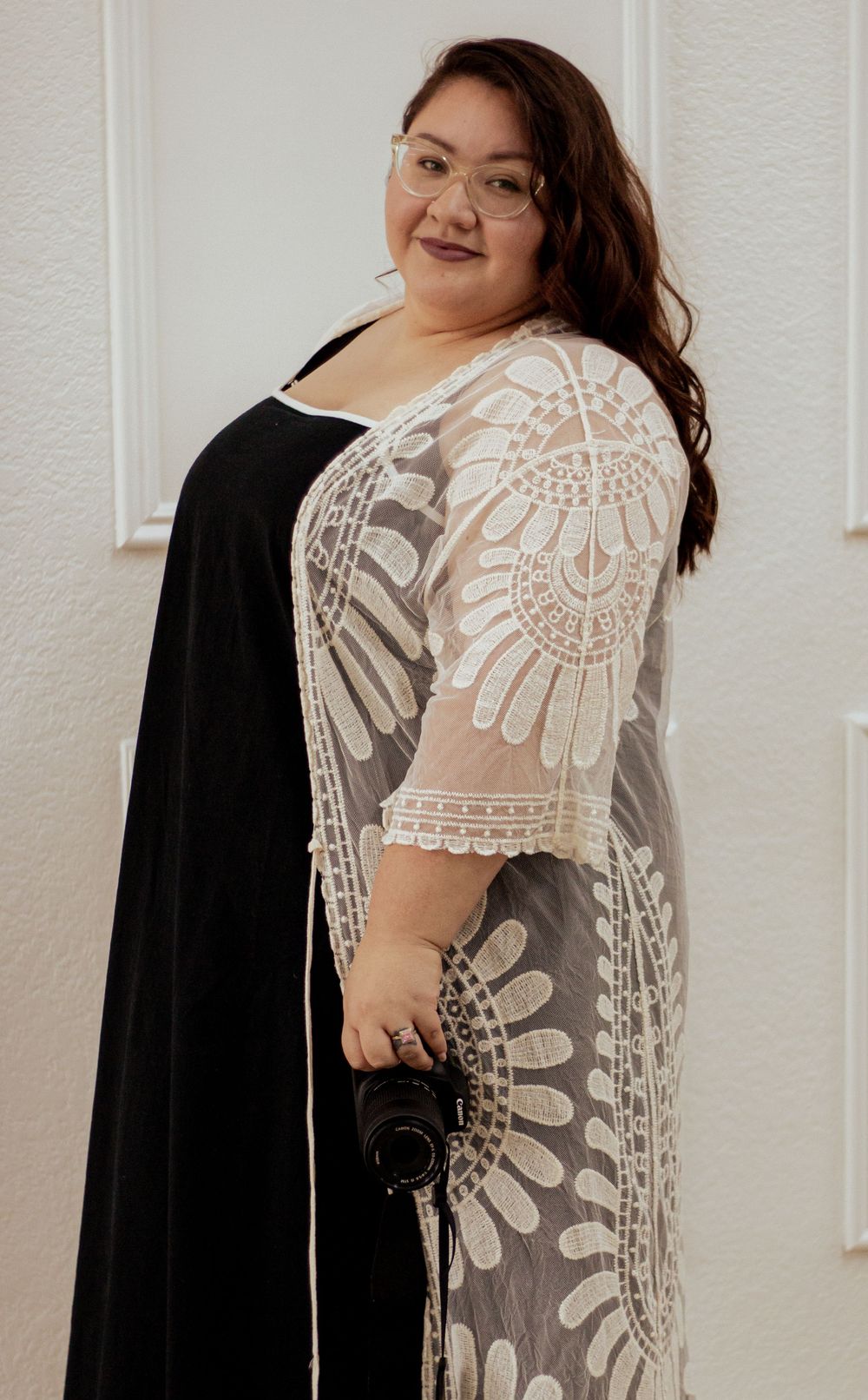 A person wearing a black dress with an elegant sheer white lace overlay featuring floral patterns and geometric designs.