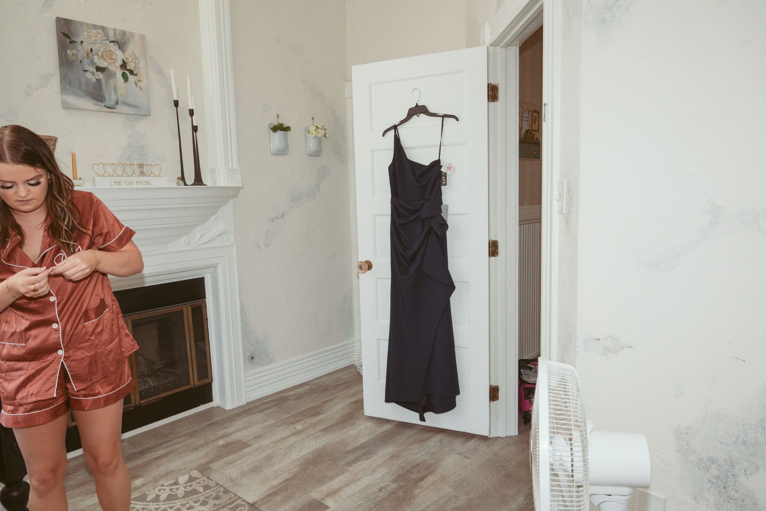 Dark bridesmaid dress hanging on door in bridal preparation room with rustic decor.