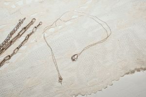 Delicate gold necklace with small pendant displayed on textured white fabric background.