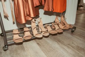 Row of neutral beige sandals lined up on wooden floor with silk robes hanging above.