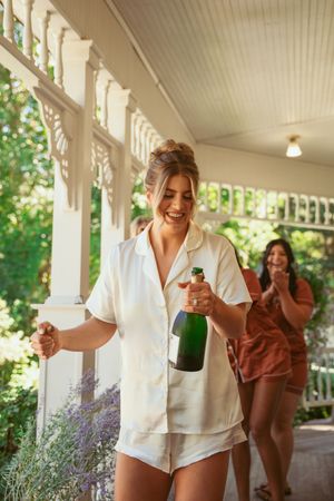 Getting ready scene on a porch with women in matching silk pajama sets celebrating with champagne.