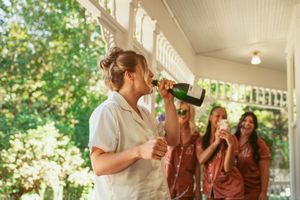 Someone taking a celebratory drink on porch while others watch in background during wedding preparations.