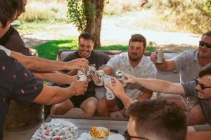 Friends toasting with bottles and drinks while celebrating together at an outdoor gathering.