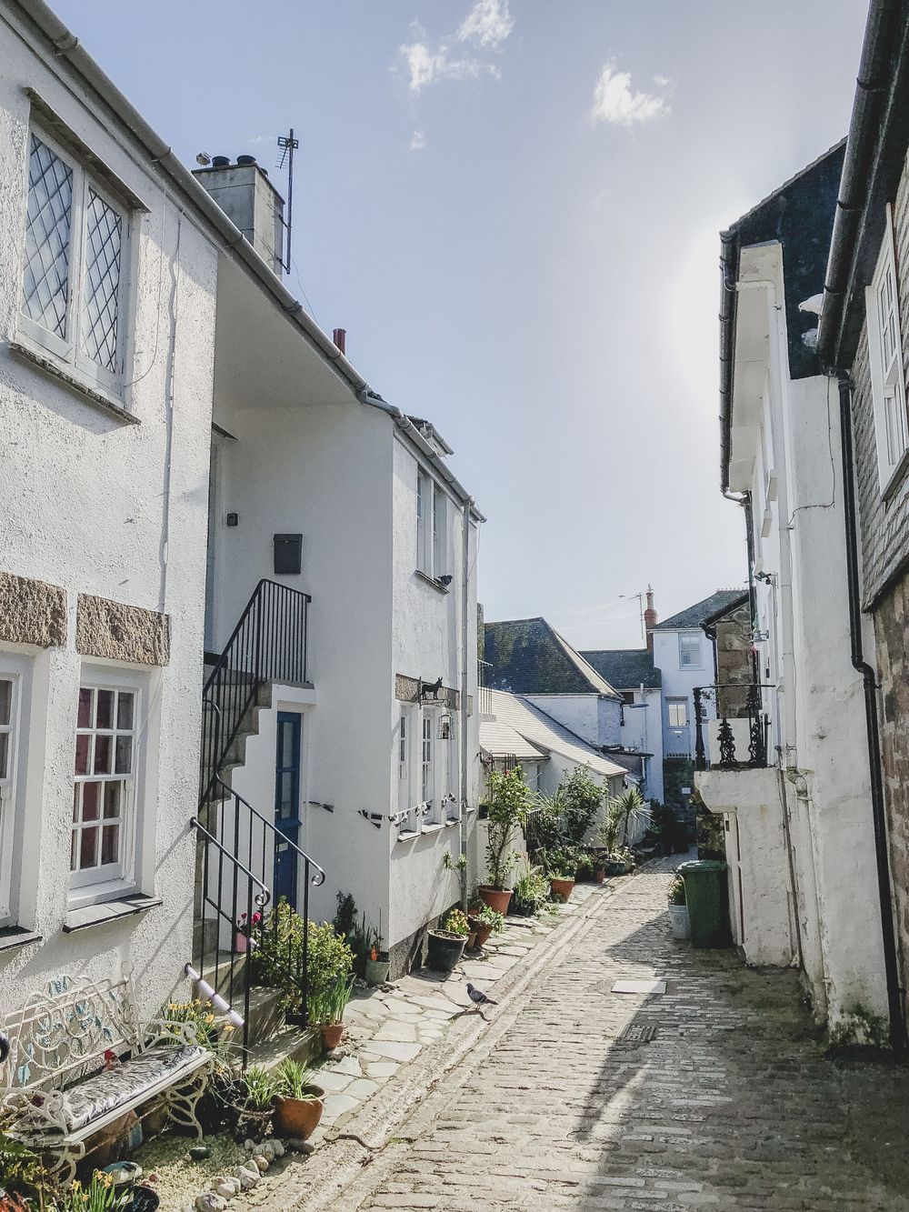 Charming stone and white cottages with blue doors line a gravel path in a quaint coastal village.