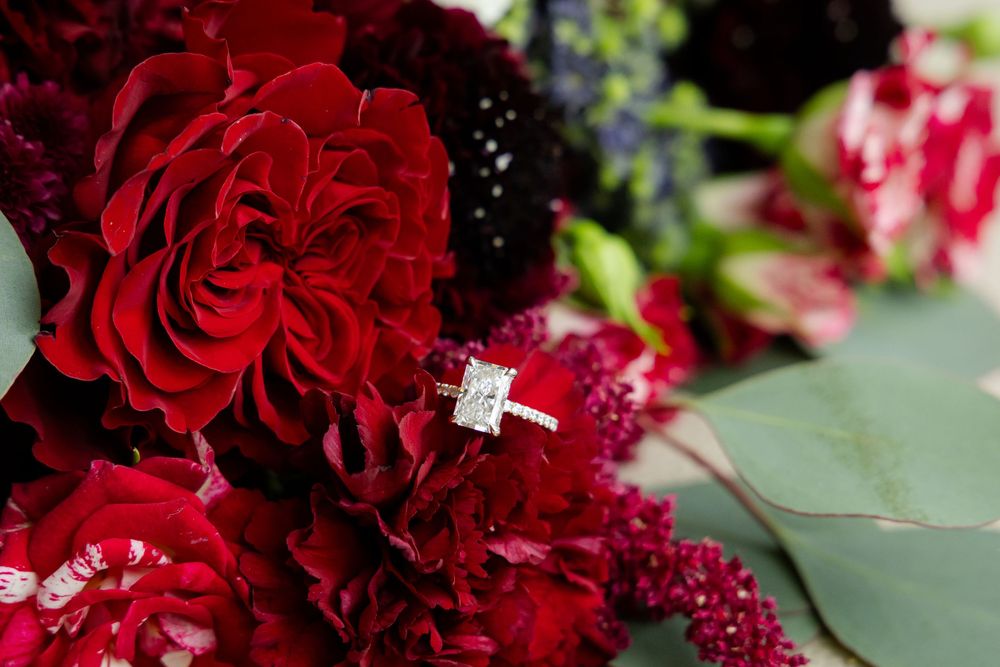 Diamond engagement ring nestled among deep red roses and floral arrangements.