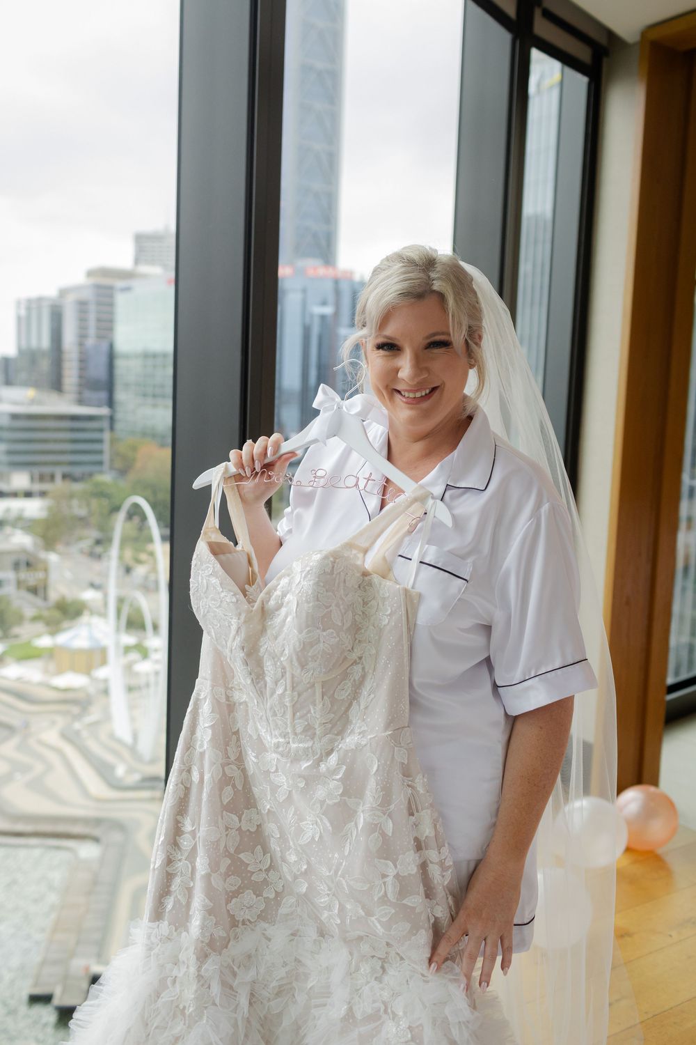Bride standing by window overlooking city skyline.
