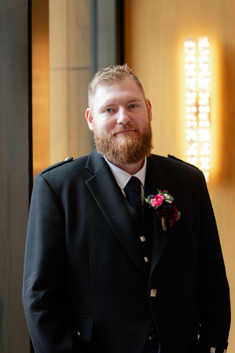 A photograph of a Groom standing by warm lighting. Scottish Wedding
