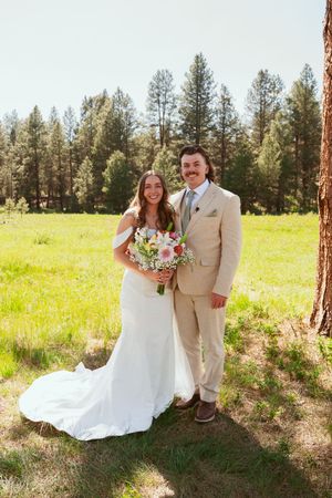 Wedding portraits captured between tall pine trees in sunlit meadow with flowing white dress.