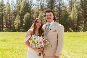 A cheerful wedding portrait in a sunny mountain meadow with pine trees.