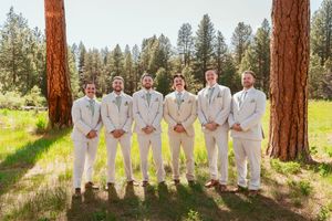 Group in coordinated cream-colored attire stands in line against rustic pine tree backdrop.