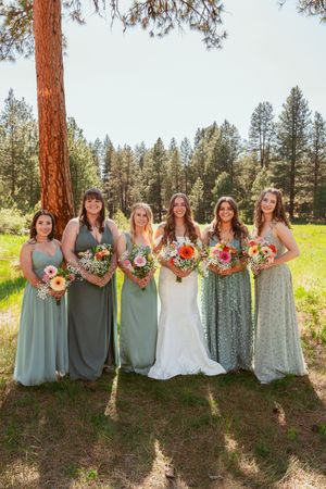 Wedding party with bridesmaids in sage green and floral dresses posing together in a forest setting.