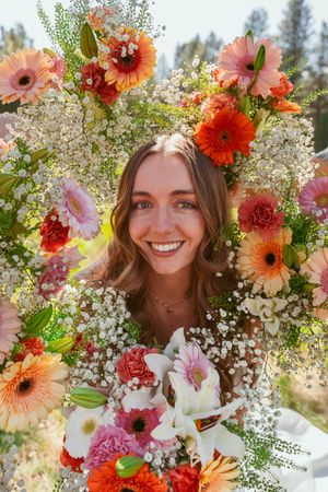Vibrant floral crown features coral gerbera daisies, baby's breath, and pink blooms in natural light.