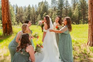 Wedding party celebrates joyfully in a sunlit forest clearing with pine trees in the background.
