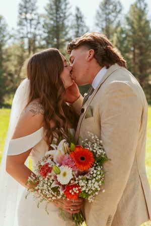Romantic outdoor wedding moment with white baby's breath and red gerbera daisy bouquet against evergreen forest backdrop.