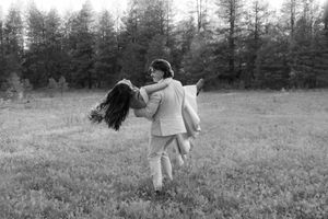 A joyful couple spins together in a meadow, captured in black and white.