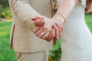 Intimate close-up of newlyweds holding hands against green grass background.