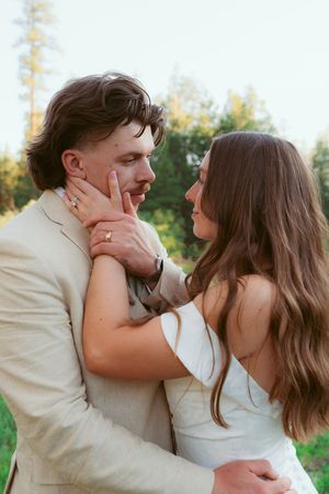A tender moment between newlyweds in formal attire against a natural forest backdrop.