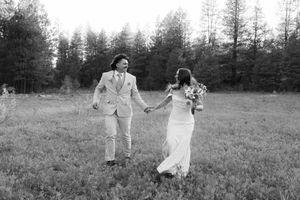 Black and white photo of people walking through a meadow surrounded by pine trees.