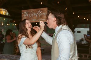 Couple sharing cake at their wedding reception under a wooden sign.