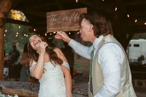 A couple laughs together during their reception under a rustic wooden sign.
