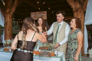 Wedding guests gather around a dessert table at a rustic barn reception with twinkling lights overhead.