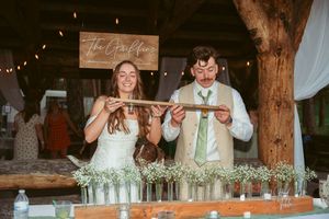A couple shares a playful moment while pouring drinks at their rustic outdoor wedding reception.