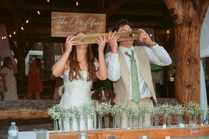 Wedding reception table with mason jars and string lights under wooden beams.