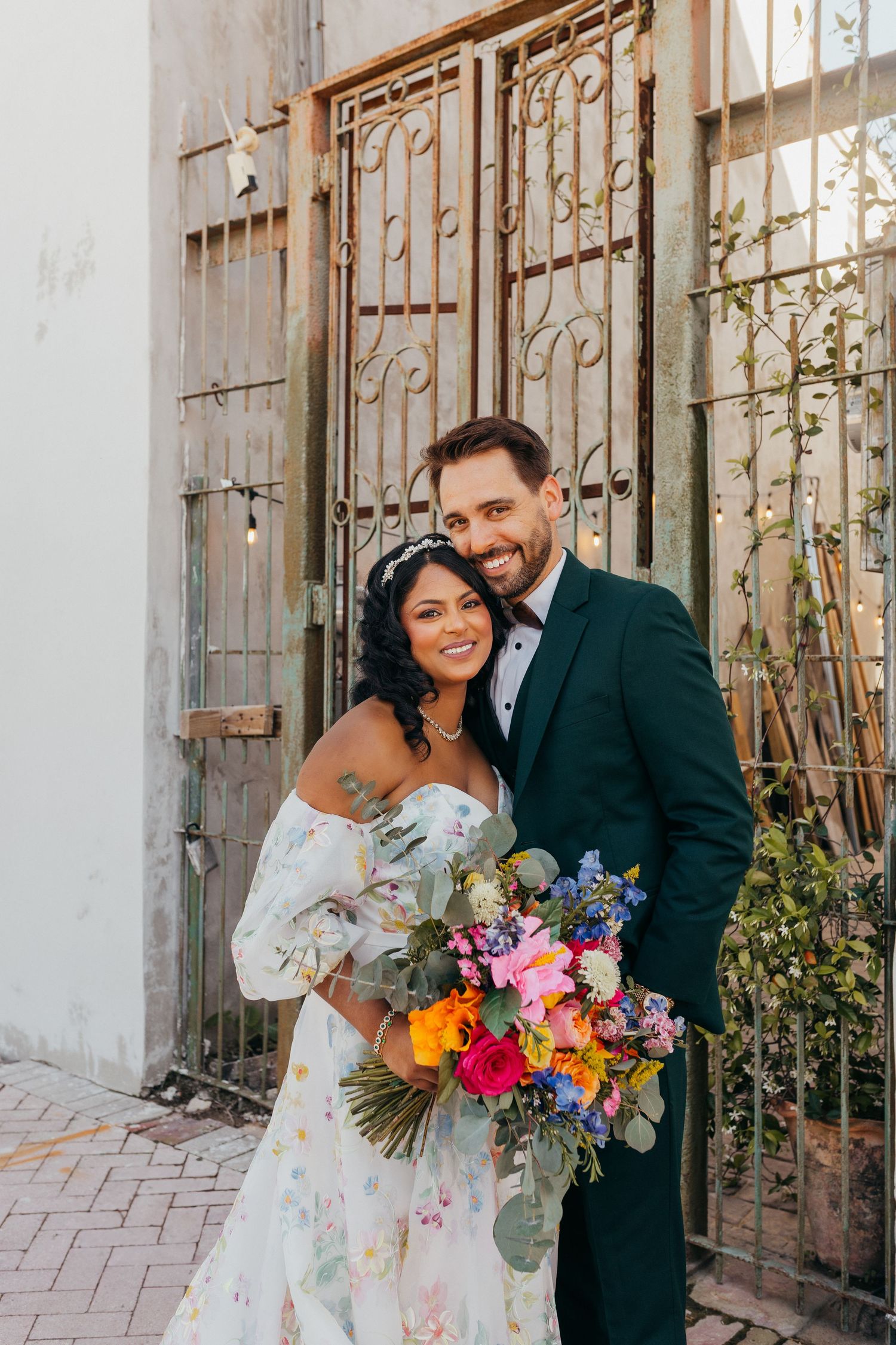 A couple share a joyful moment in front of a rustic door with stained glass windows during their wedding celebration.