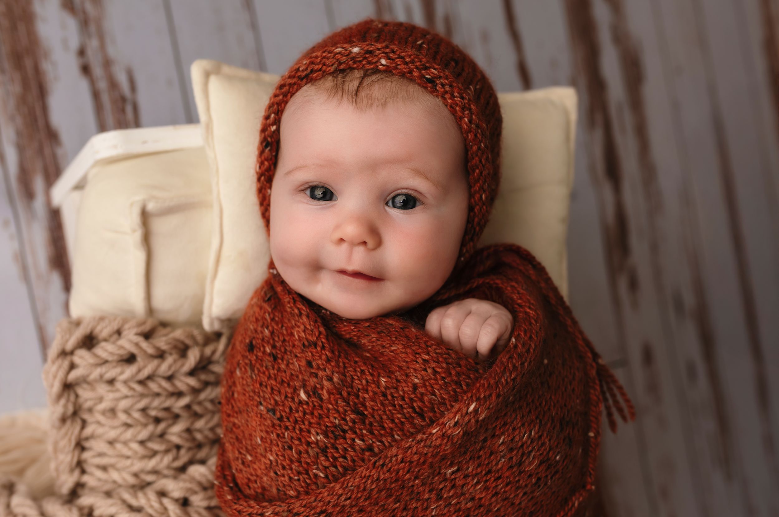 Charlottesville photographer, newborn, family, baby, and maternity; bright-eyed newborn wrapped in an orange knit blanket smiles.