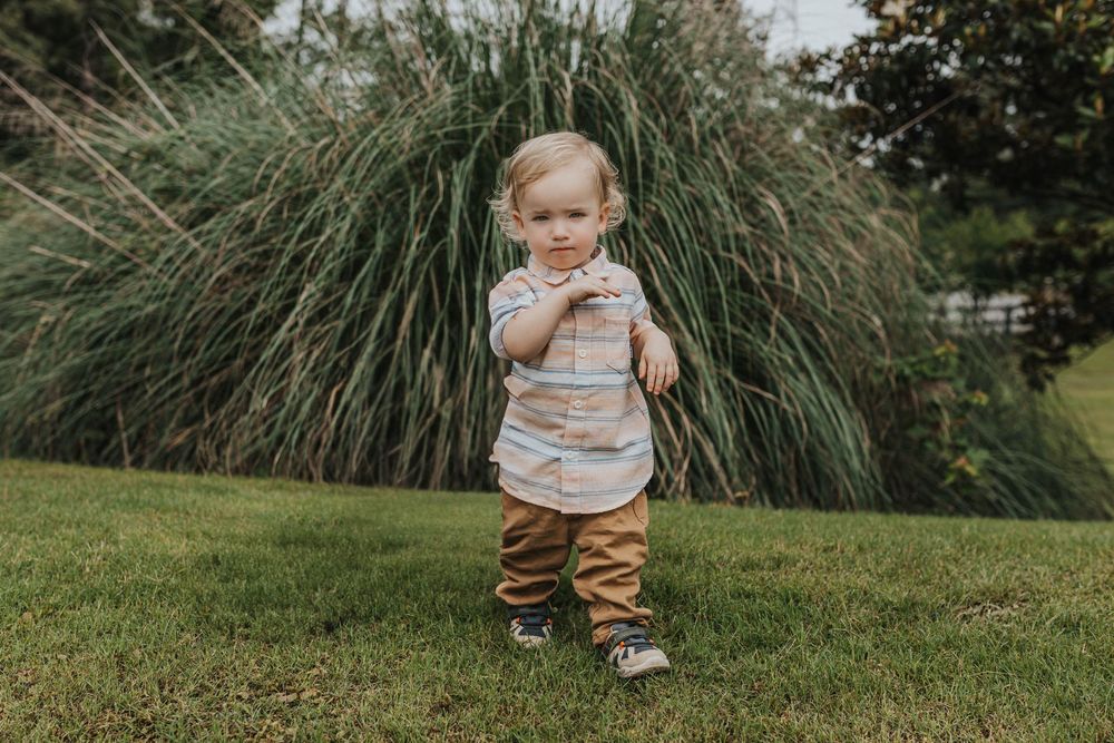 Child walking on grass near ornamental grasses during outdoor photo session.