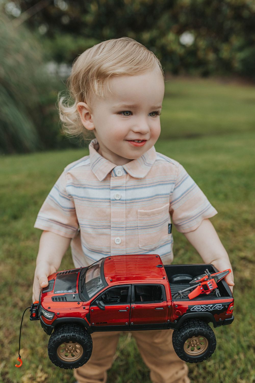 Toddler playing with red toy truck on grass during outdoor photoshoot.