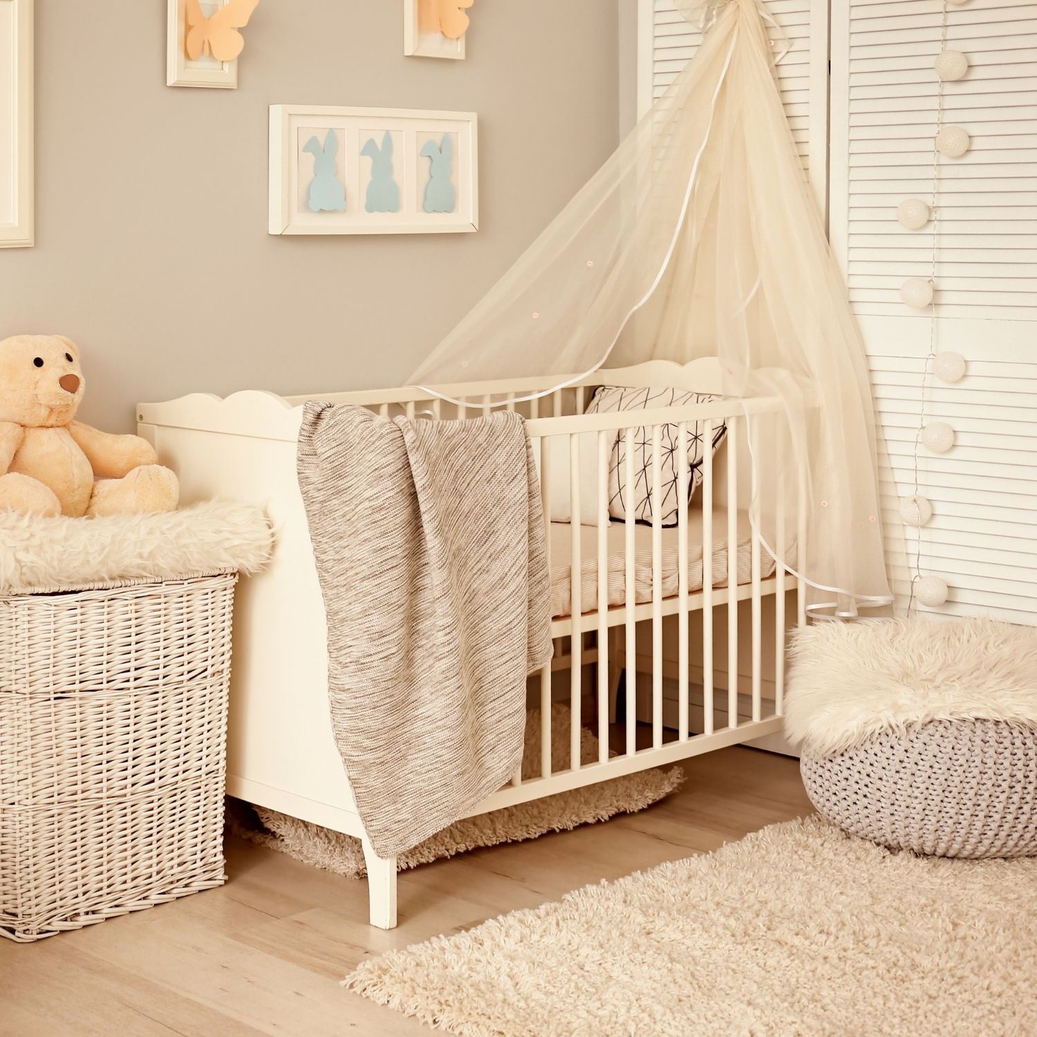Warm tones nursery with a white crib, laundry basket with a teddy bear on it and a seat next to the crib.