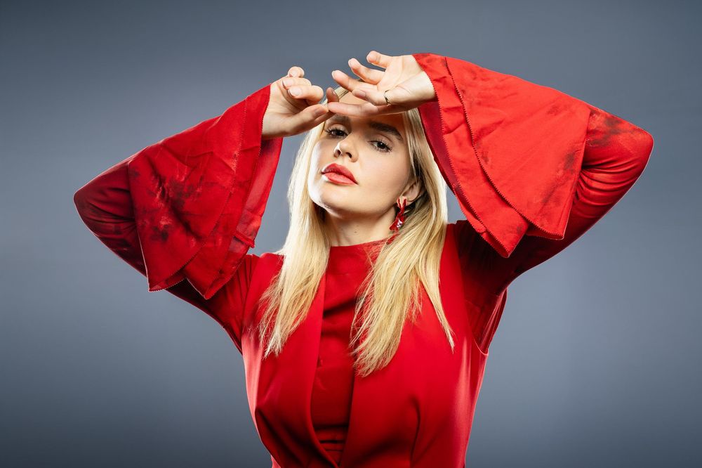 Dramatic pose in vibrant red sweater against studio backdrop.