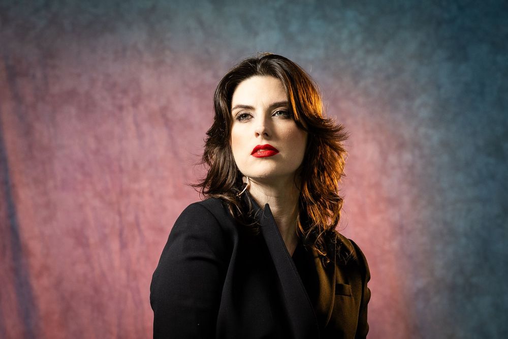 Studio fashion series showing elegant black coat styling against pink and blue backdrop.