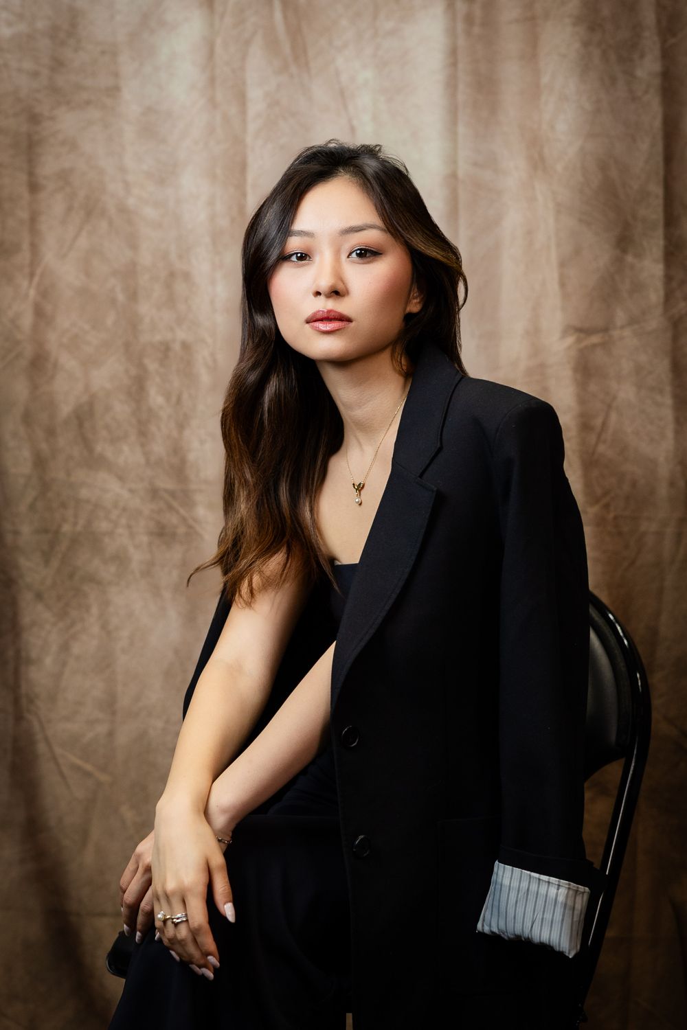 Professional studio portrait of woman in black blazer against textured beige backdrop.