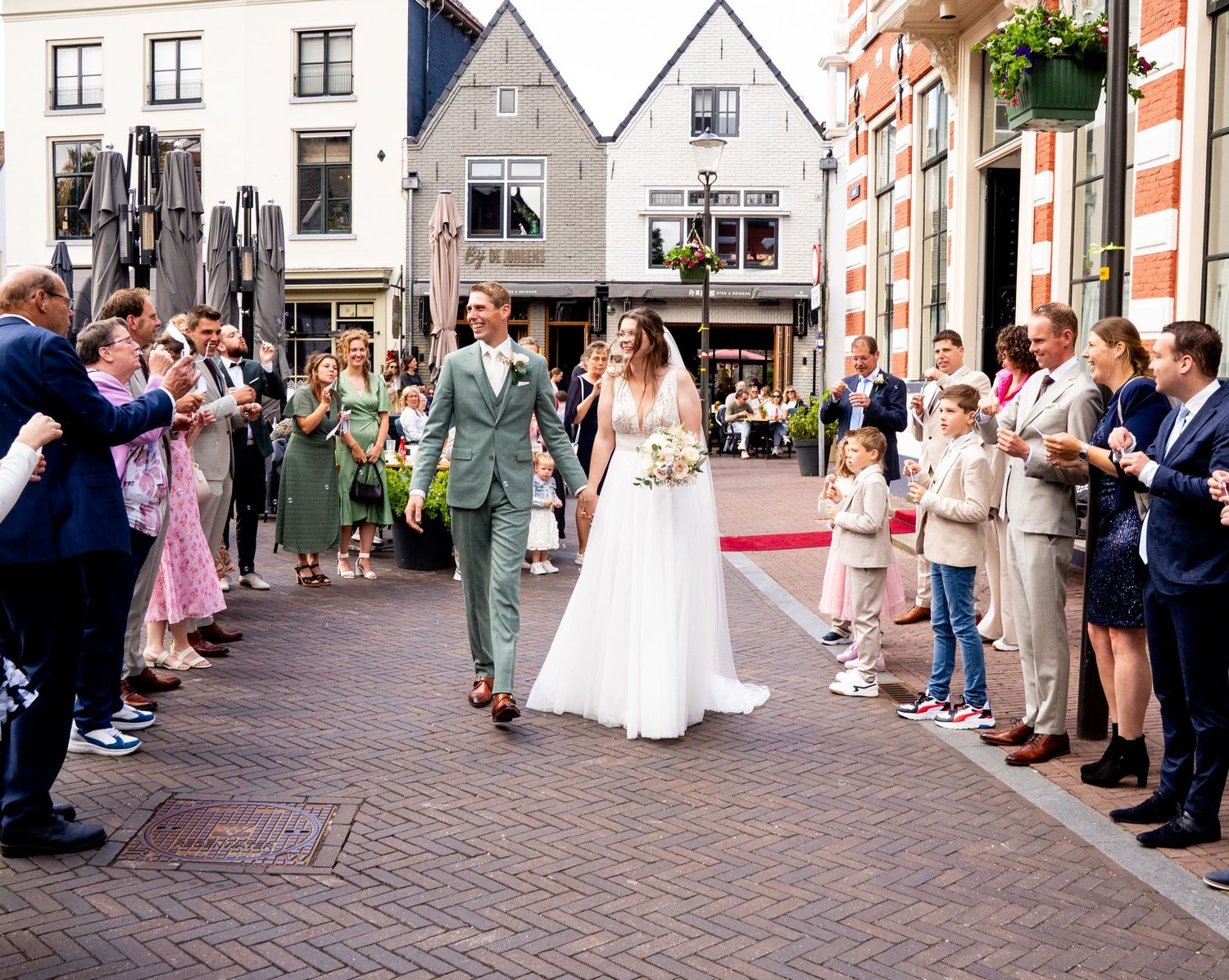 Bruidspaar loopt weg van het stadhuis in Hattem en wordt ontvangen door hun familie met bellen blazen